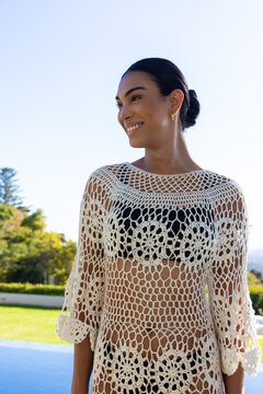 African American woman standing by pool wearing crochet cover-up over black bikini, gold earring