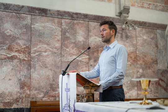 Preacher standing behind a pulpit with a microphone in a church, reading from a Bible to deliver a sermon, homily, or lead prayer.