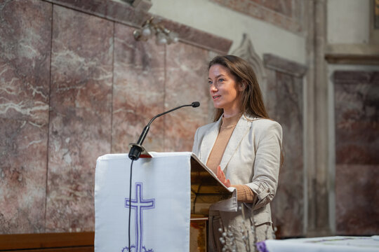 Woman lector in the Catholic Church, standing behind the pulpit and reading Scripture on a microphone, to the congregation at Mass.