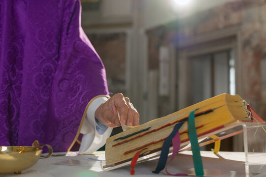 Priest in a purple vestment, a chasuble, turning pages in a Missal, a liturgical book of the Eucharistic prayer during Catholic Mass.
