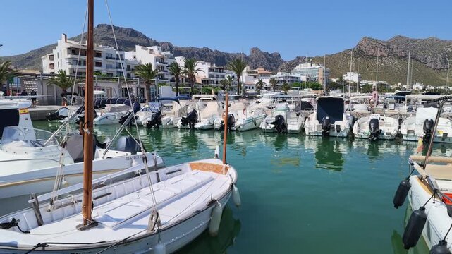 Port de Pollenca Mallorca Spain. 01.06.2026. Video. A serene view of a bustling harbor filled with various boats under a clear blue sky, with picturesque mountains framing the coastal town