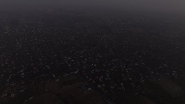 A high altitude aerial panorama of a scenic Armenian town split by a deep rocky canyon, showcasing houses, autumn trees, and distant misty mountains under a hazy sky.

