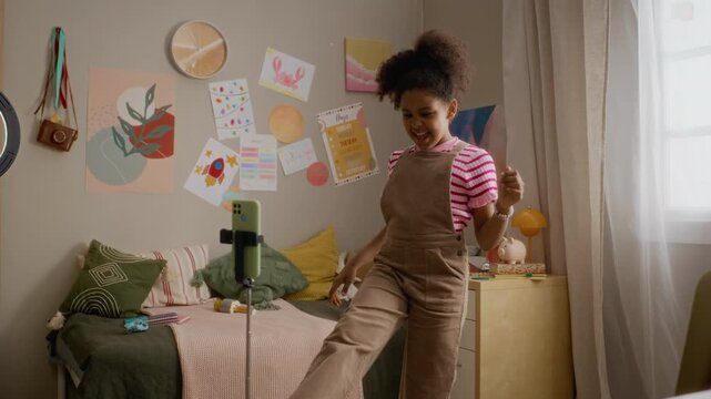 African American child dancing in front of smartphone on tripod, accidentally knocking it over. Footage representing social media bloopers, kid influencer fails, and digital lifestyle