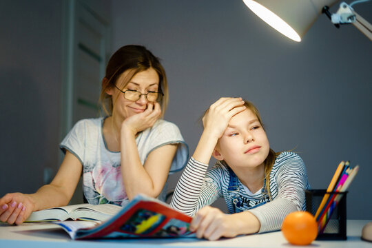 Mother helping her tired daughter with homework at home.