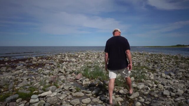 Lange Erik, Sweden A man walks on the rocky and grassy Baltic Sea shore on the northern tip of the Oland island in summer.