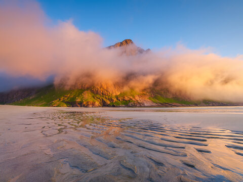 Norwegian arctic fjord at midnight sun. Lofoten Islands, Norway. Arctic landscape with mountains, beach and golden clouds. Scenic Nordic nature with summer night light and mountain peaks.