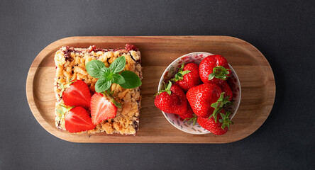 Sweet homemade pie with strawberry jam, decorated with fresh strawberries and aromatic herbs on the wooden tray on dark stone background top view. © Iryna