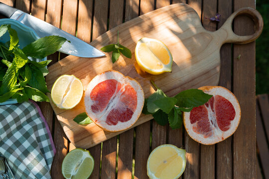 High angle flat lay of fresh cut grapefruits, lemons, limes and mint on a wooden cutting board for summer cocktail