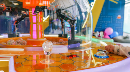 Child's hand operating a claw machine game with colorful lights and prizes inside © shine.graphics