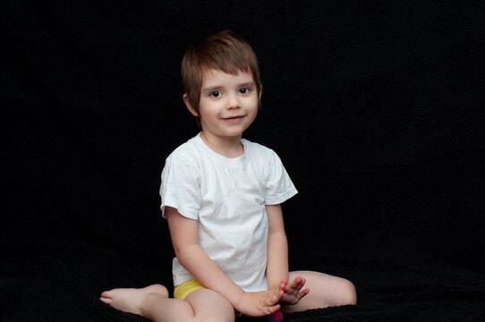 Child sits on the floor with a smile in a simple indoor setting during the day