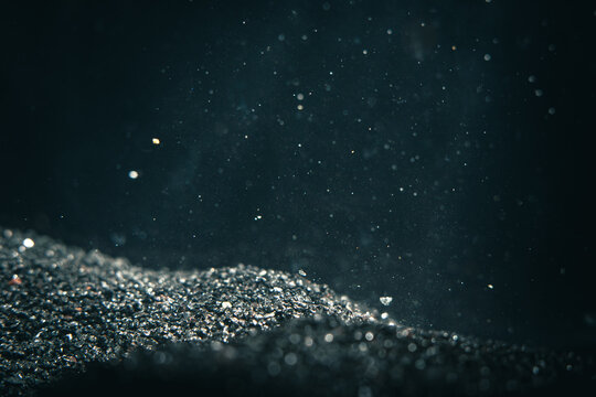 Dust particles float in the air from the surface of black sand in a dark setting