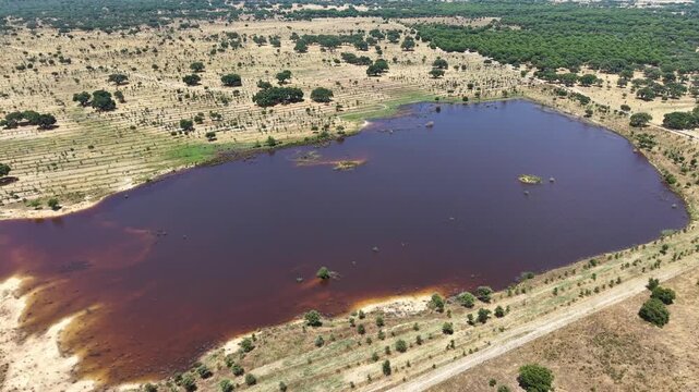 Aerial arc shot of lake surrounded by dry, semi-arid landscape with distinct agricultural