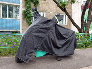 Black nylon motorcycle cover shielding a parked motorbike in a quiet residential yard near a multi story building ensuring protection from weather and dust exposure © Harmony Video Pro