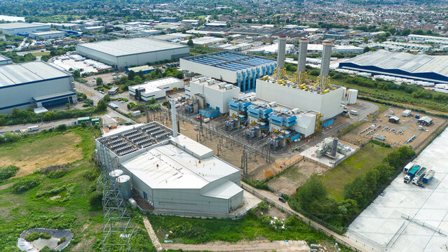 Aerial view of Rye House Power Station with its cooling towers and industrial infrastructure surrounded by warehouses and green fields in Hoddesdon, England, United Kingdom.