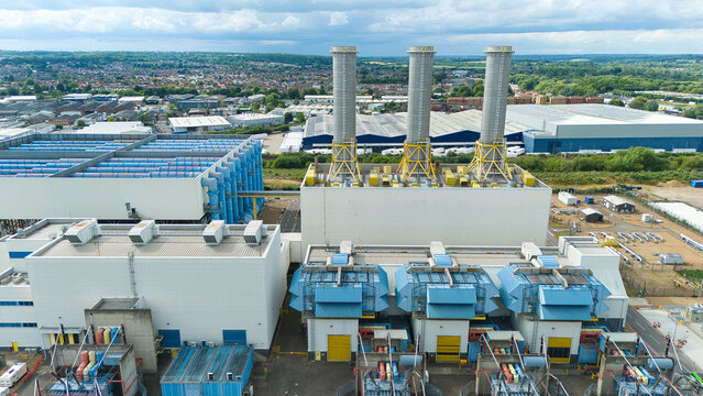 Aerial view of Rye House Power Station featuring three prominent chimneys and industrial infrastructure surrounded by warehouses and greenery in Hoddesdon, England, United Kingdom.