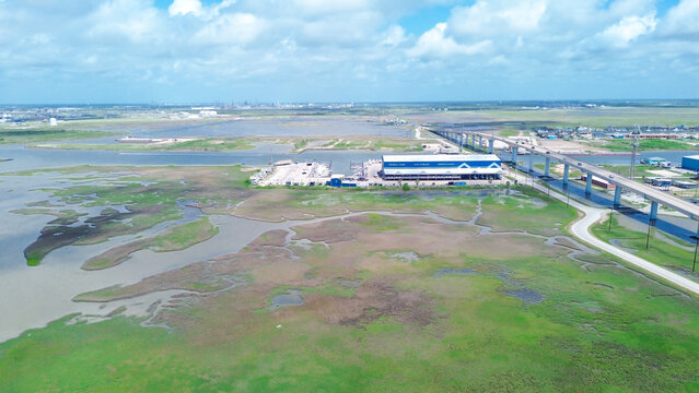 Modern marine storage facility sits adjacent to bridge infrastructure. Winding tidal channels cut through green marsh, supporting maritime focused economy, Freeport, TX