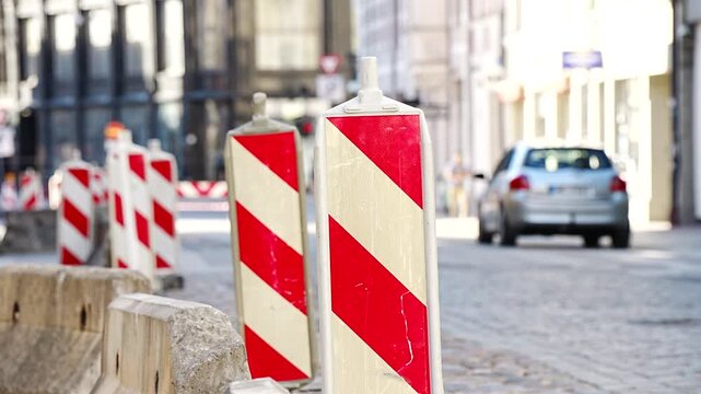 Row of vertical red and white striped traffic barriers on concrete blocks placed along a cobblestone street for road construction safety