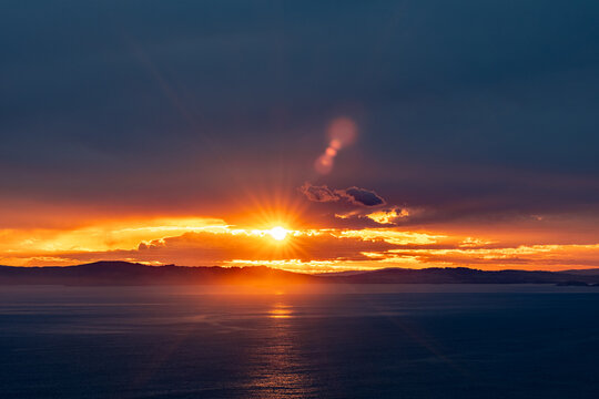 Aerial view of the sun setting over the ocean with dramatic clouds and a distant coastline visible from Sharp Point Lookout in Torndirrup, Western Australia, Australia.