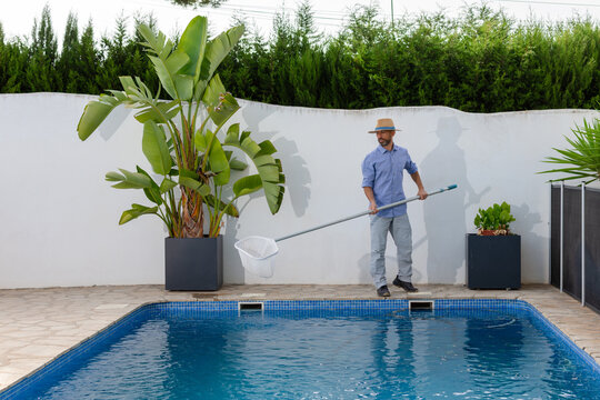 Pool cleaning worker lifting skimmer net full of debris from swimming pool