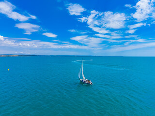 Obraz premium Sailing on clear blue water under a bright sky with clouds and distant land by the shore during a sunny day