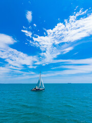 Fototapeta premium Sailing on clear blue waters under a bright sky with clouds at midday in a serene coastal area