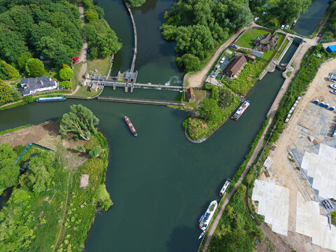 Aerial view of Feildes Weir Lock on the River Lee, featuring narrowboats navigating the waterway, lush green trees, and surrounding rural landscape in Hoddesdon, England, United Kingdom.