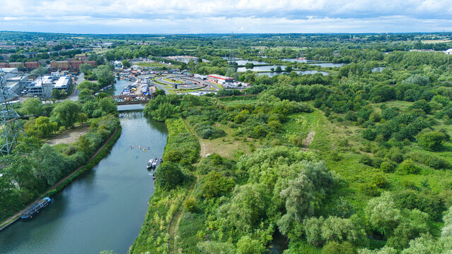 Aerial view of Feildes Weir Lock on the River Lee with lush green vegetation, a nearby go-kart track, and narrowboats moored along the waterway, Hoddesdon, England, United Kingdom.