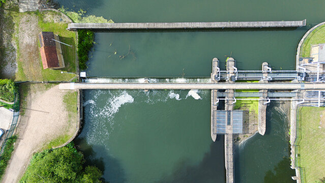 Aerial view of Feildes Weir Lock No.5 with water flowing over the weir, concrete structures, and green banks in Hoddesdon, England, United Kingdom.