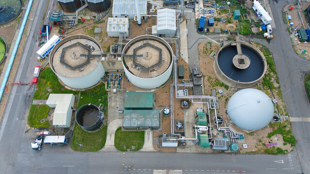 Aerial view of the Alpheus Wastewater Sewage Treatment works featuring large circular sedimentation tanks, industrial piping, and a storage dome in Milton Keynes, England, United Kingdom.