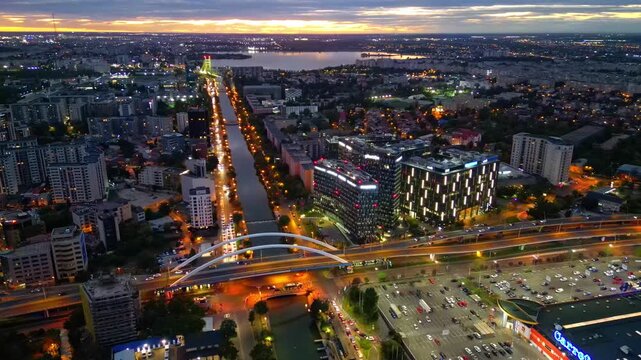 Drone aerial footage of a spectacular sunset in Bucharest, Romania. The camera captures the scenic Dambovita River in the Orhideea business area, showcasing modern office buildings, vibrant golden hou