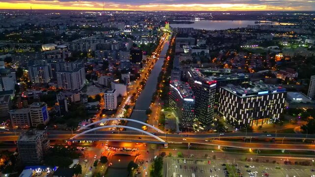 Drone aerial footage of a spectacular sunset in Bucharest, Romania. The camera captures the scenic Dambovita River in the Orhideea business area, showcasing modern office buildings, vibrant golden hou