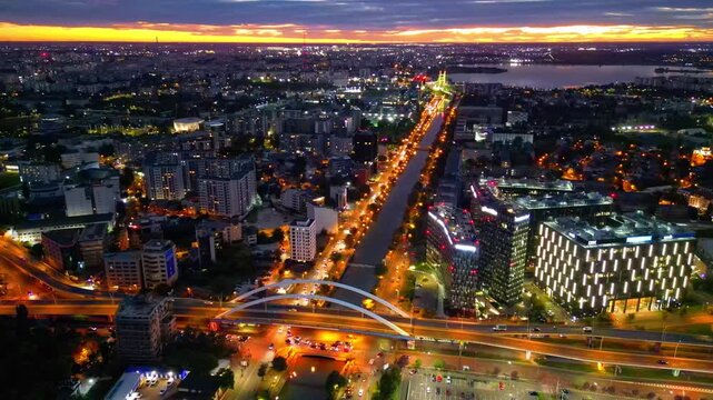 Drone aerial footage of a spectacular sunset in Bucharest, Romania. The camera captures the scenic Dambovita River in the Orhideea business area, showcasing modern office buildings, vibrant golden hou
