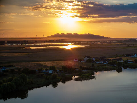 Aerial view of Murighiol Delta Dunarii at sunset with golden light reflecting on the water, surrounding wetlands, and distant hills in Murighiol, Judetul Tulcea, Romania.