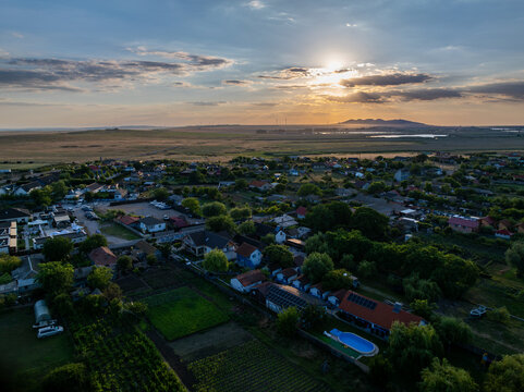 Aerial view of the village of Murighiol near the Danube Delta, featuring houses, gardens, a swimming pool, and fields under a golden sunset sky in Murighiol, Judetul Tulcea, Romania.