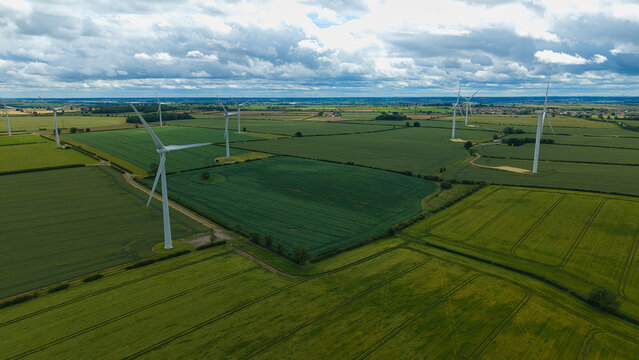 Aerial view of Burton Latimer Wind Turbines set amidst lush green agricultural fields under a cloudy sky in Burton Latimer, England, United Kingdom.