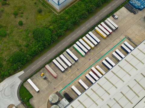 Aerial view of Corby Gate Business Park featuring rows of parked semi-trailers, a large warehouse facility, and adjacent green space in Corby, England, United Kingdom.