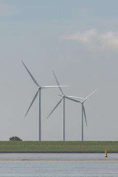 Breskens, Netherlands. Three wind turbines along the Westerschelde estuary with navigation buoy and sandbank highlighting renewable energy infrastructure