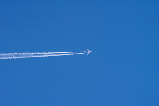 Airplane at high altitude with contrails in clear blue sky