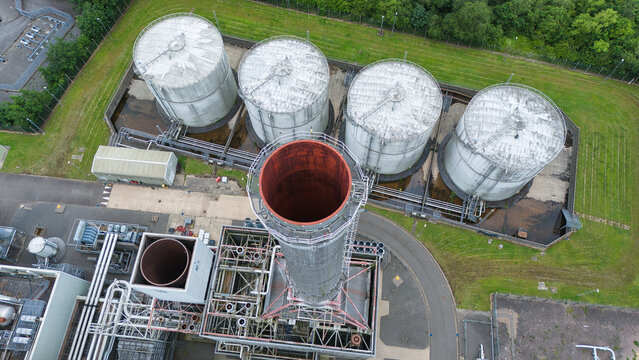 Aerial view of Corby Power Station featuring a prominent tall chimney stack and large industrial storage tanks surrounded by green vegetation in Corby, England, United Kingdom.