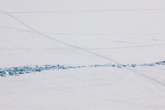 Aerial view of the frozen surface of Lake Baikal with blue ice ridges and snowmobile tracks across the white landscape in Baikalskoye, Buryatia, Russia.