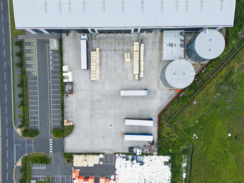 Aerial view of a logistics warehouse facility with loading bays, parked semi-truck trailers, large storage tanks, and pallets of goods in Corby, England, United Kingdom.