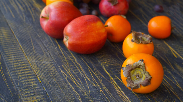 Close up of ripe persimmon with red apples on dark wooden table with copy space.