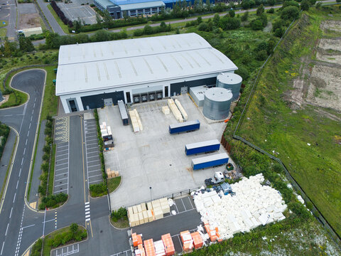 Aerial view of a modern industrial warehouse facility with loading docks, parked semi-trailers, and storage areas in Corby, England, United Kingdom.