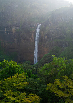 Aerial view of Cikanteh Waterfall cascading down a lush cliffside surrounded by dense tropical forest and mist in Geopark Ciletuh, West Java, Indonesia.
