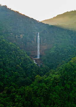Aerial view of Cikanteh Waterfall cascading down a lush green cliff face surrounded by dense tropical rainforest in Geopark Ciletuh, West Java, Indonesia.