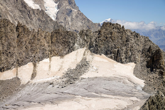 Aerial view of the rugged alpine landscape and glacier seen from Punta Helbronner, featuring sharp rocky peaks and snow-covered slopes in Courmayeur, Aosta Valley, Italy.