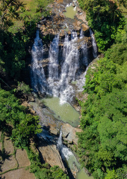 Aerial view of Cigangsa Waterfall cascading over rocky cliffs surrounded by lush tropical vegetation and dense forest in West Java, Indonesia.