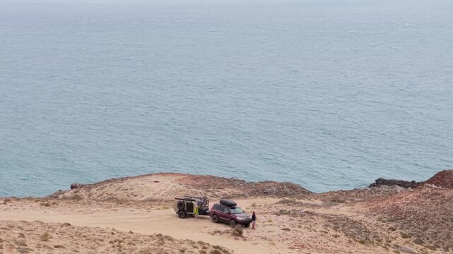 Suv and teardrop camper trailer set up on a cliff overlooking the pacific ocean during an overland trip in baja california.