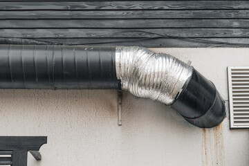 Naklejka premium Exterior of an industrial building showing a black ventilation pipe connecting to a silver flexible duct on a textured wall