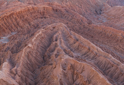 Aerial view of the rugged, arid landscape of the Atacama Desert featuring deep ridges and textured red rock formations, located in San Pedro de Atacama, Antofagasta, Chile.